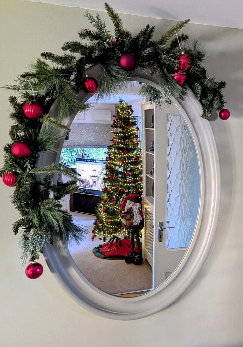 Mirror with a Christmas garland reflecting a room with a Christmas tree and festive decorations.