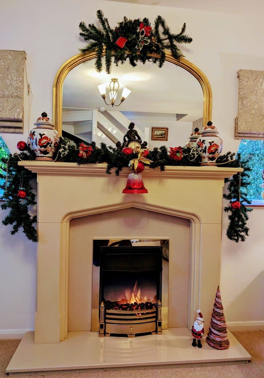 Festive fireplace with garlands, ornaments, mirror, and Santa figurine on the hearth.