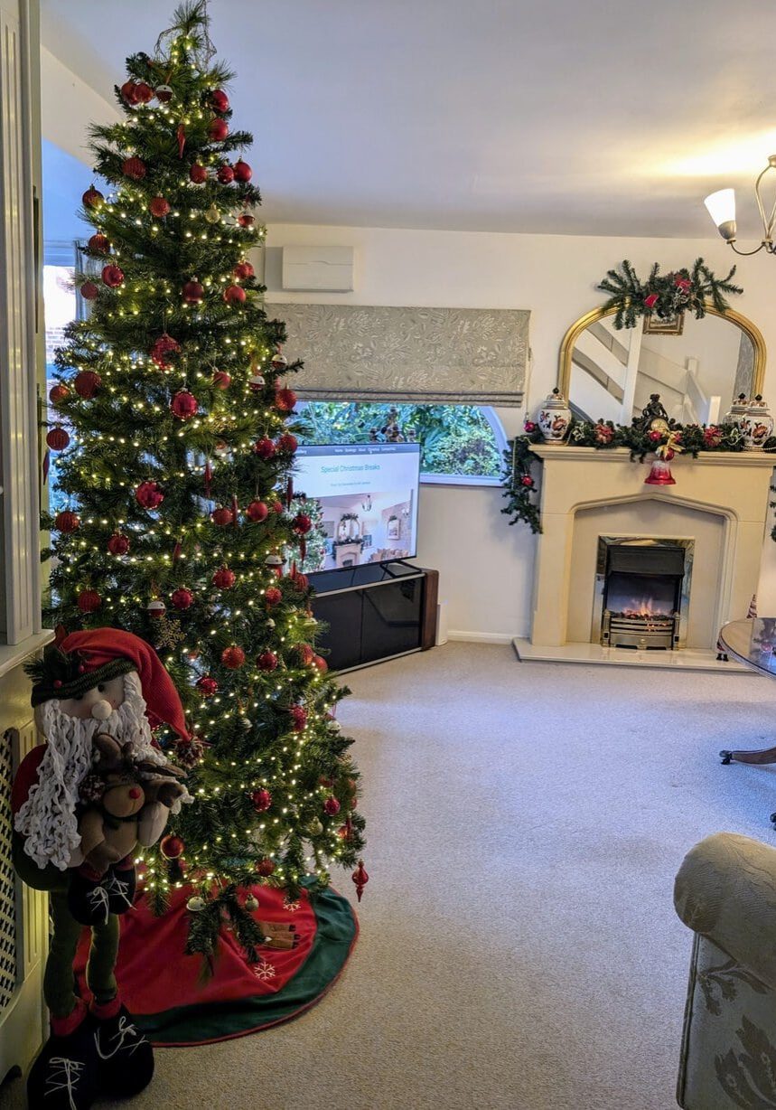 Living room decorated for Christmas with a tree, Santa figure, garlands, red bows and mirror.