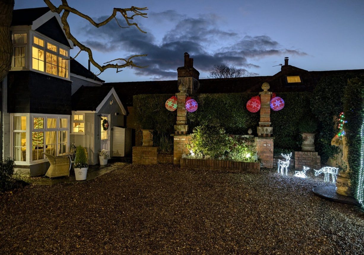 The Cottage at Christmas with lights, reindeer, a tree, wreath, and large red ornaments.