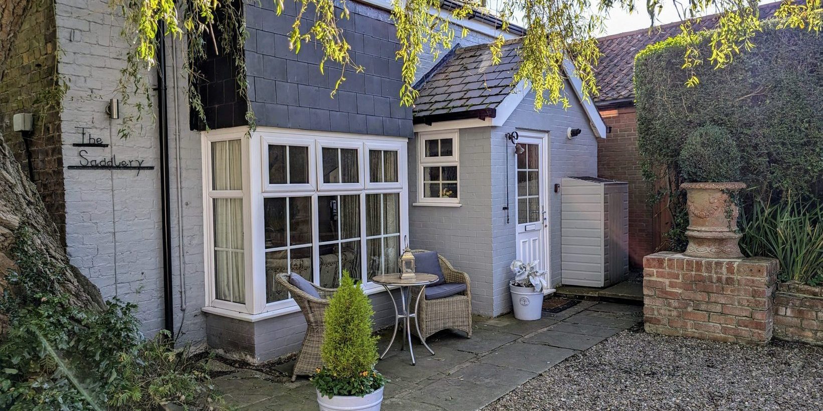 Front view of the cottage with flagstone patio, two comfortable chairs and table and two planters.